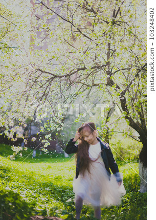 Little girl in black jacket and white dress dancing in the spring cherry garden 103248402