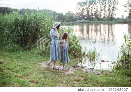 A girl stands on the shore of the lake and looks at nutria in the water A girl stands on the shore of the lake and looks at nutria in the water 103248407