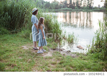 A girl stands on the shore of the lake and looks at nutria in the water A girl stands on the shore of the lake and looks at nutria in the water 103248411