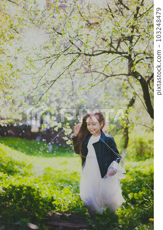 Little girl in black jacket and white dress dancing in the spring cherry garden Little girl in black jacket and white dress dancing in the spring cherry garden 103248479