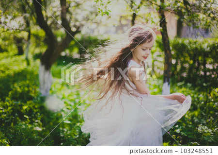 Little girl in long white dress dancing in the spring cherry garden Little girl in long white dress dancing in the spring cherry garden 103248551