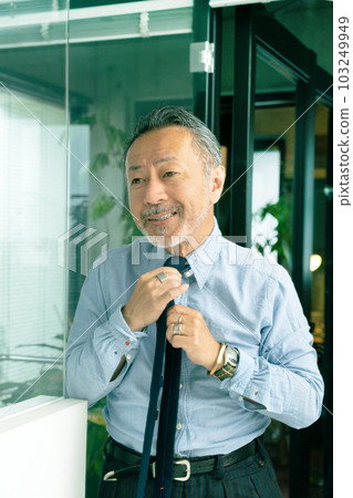 Middle-aged man looking in the mirror and tying his tie Vertical position Middle-aged man looking in the mirror and tying his tie Vertical position 103249949