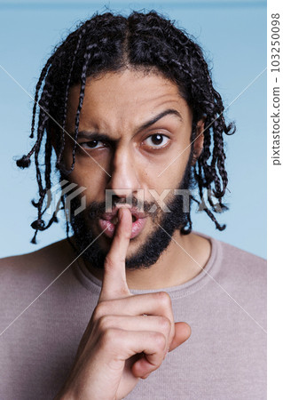 Irritated arab man making shh sign with serious face expression and looking at camera. Person showing silence gesture with finger, raising eyebrow and holding forefinger on lips portrait Irritated arab man making shh sign with serious face expression and looking at camera. Person showing silence gesture with finger, raising eyebrow and holding forefinger on lips portrait 103250098