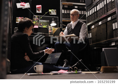 Private detective analyzing suspect evidence on laptop computer, working late at night at criminal investigations with police officer. Overworked investigators checking victim report Private detective analyzing suspect evidence on laptop computer, working late at night at criminal investigations with police officer. Overworked investigators checking victim report 103250199