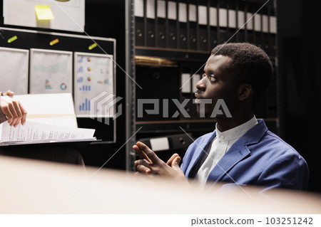 Police officers discussing criminal case, working overtime at federal investigation in arhive room. Diverse private investigators analyzing crime scene evidence, discovering mysterious suspect 103251242
