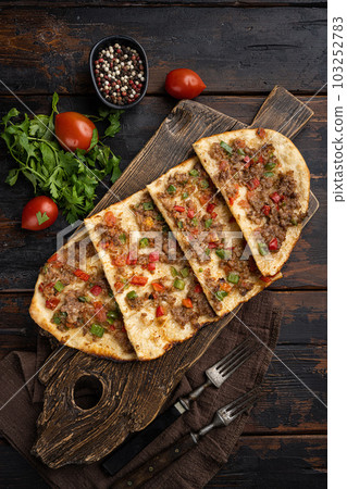Turkish pide with minced lamb, tomatoes, bell pepper, on old dark  wooden table background, top view flat lay 103252783