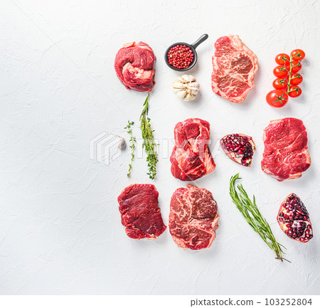 Rraw beef steaks set top blade, rump, chuck eye roll with herbs pomegranate over white concrete background, top view space for text. Rraw beef steaks set top blade, rump, chuck eye roll with herbs pomegranate over white concrete background, top view space for text. 103252804