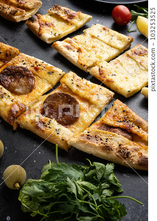 Pide, sucuklu pide Turkish pide with sausage, on black dark stone table background 103253525