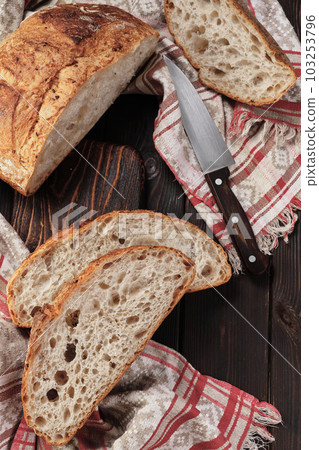 Round rustic bread without kneading cut into pieces on a cutting board on an old dark rustic table. Homemade whole grain bread, layout on the table, vertical frame 103253796