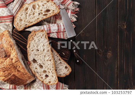 Sliced round rustic bread without kneading on a cutting board on an old rustic table with copy space, dark background. Homemade whole grain bread, layout on the table 103253797