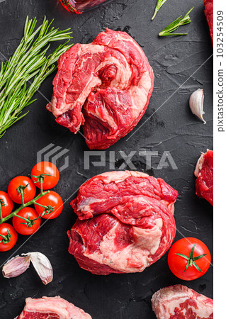 Raw chuck eye roll beef steak cuts, with herbs, seasoning on black table, top view. Raw chuck eye roll beef steak cuts, with herbs, seasoning on black table, top view. 103254509