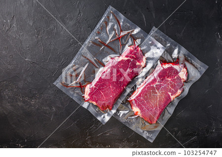 Rump steak in vacuum sealed bag on black textured background, side view space for price. Rump steak in vacuum sealed bag on black textured background, side view space for price. 103254747