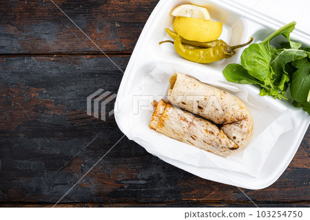Traditional Turkish cuisine doner kebab, in plastic pack container delivery lunch box, on old dark  wooden table background, top view flat lay, with copy space for text 103254750