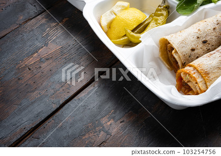 Doner kebab wrap in lavash bread, in plastic pack container delivery lunch box, on old dark wooden table background, with copy space for text Doner kebab wrap in lavash bread, in plastic pack container delivery lunch box, on old dark wooden table background, with copy space for text 103254756