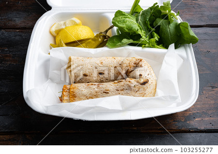 Street food chicken tantuni Turkish doner, in plastic pack container delivery lunch box, on old dark wooden table background Street food chicken tantuni Turkish doner, in plastic pack container delivery lunch box, on old dark wooden table background 103255277