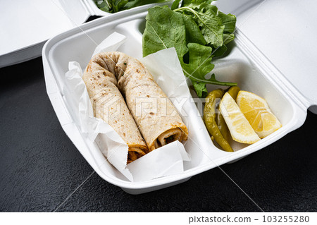 Traditional Turkish cuisine doner kebab, in plastic pack container delivery lunch box, on black dark stone table background Traditional Turkish cuisine doner kebab, in plastic pack container delivery lunch box, on black dark stone table background 103255280