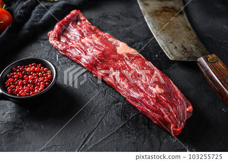 Raw machete also known as bistro steak, fajita meat or onglet, near butcher knife with pink pepper and rosemary. Black background. Side view Raw machete also known as bistro steak, fajita meat or onglet, near butcher knife with pink pepper and rosemary. Black background. Side view 103255725