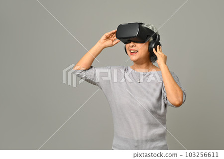 Elderly woman experiencing technology and innovation via VR headset isolated on gray background 103256611