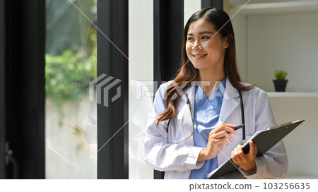 Positive female doctor in white coat holding medical form and looking out window. Healthcare and medical concept Positive female doctor in white coat holding medical form and looking out window. Healthcare and medical concept 103256635