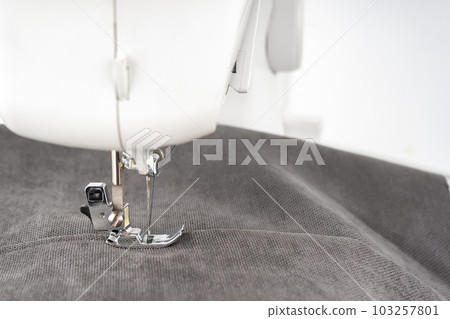 Modern sewing machine presser foot with gray fabric and thread, closeup 103257801