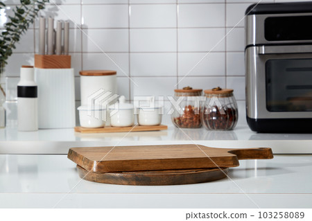 Stacked of wooden cutting board form an empty podium for display product. In the background is the counter with spice boxes, knife tray and microwave decorated on white tile background 103258089