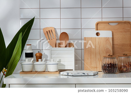 A corner of a modern kitchen with full kitchen appliances and green plants on a white tile wall background. In the middle is an empty marble podium for product presentation. A corner of a modern kitchen with full kitchen appliances and green plants on a white tile wall background. In the middle is an empty marble podium for product presentation. 103258090
