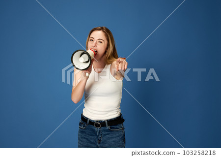 Portrait of young girl, student, influencer talking in megaphone against blue studio background. News, information 103258218