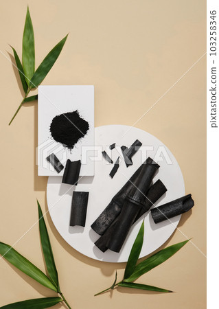 White rectangle podium with black powder stacked on round podium with activated charcoal sticks placed on. Activated charcoal can reduce the size of your pores 103258346