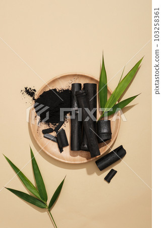 Flat lay of activated charcoal sticks and powder displayed on a round wooden dish. Activated charcoal helps detoxify and absorb excess oil 103258361
