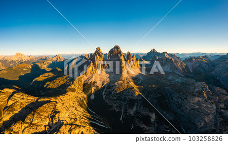 Majestic silhouette of Tre Cime di Lavaredo at sunrise. Spacious mountain landscape with rocky peaks and snow-covered slopes aerial view in back lit Majestic silhouette of Tre Cime di Lavaredo at sunrise. Spacious mountain landscape with rocky peaks and snow-covered slopes aerial view in back lit 103258826