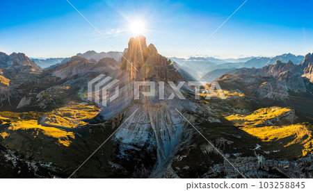 Mountain landscape of Three Peaks of Lavaredo at sunrise. Sunny jagged peaks and broad hilly shaded highlands covered with grass and sand aerial view 103258845