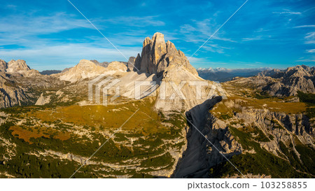 High Stone Columns and Battlement-Like Peaks of Tre Cime di Lavaredo's Mountain Massif, Enveloped in the Golden Hues of Sunset, Underneath a Breathtaking Blue Sky with White Clouds. High Stone Columns and Battlement-Like Peaks of Tre Cime di Lavaredo's Mountain Massif, Enveloped in the Golden Hues of Sunset, Underneath a Breathtaking Blue Sky with White Clouds. 103258855