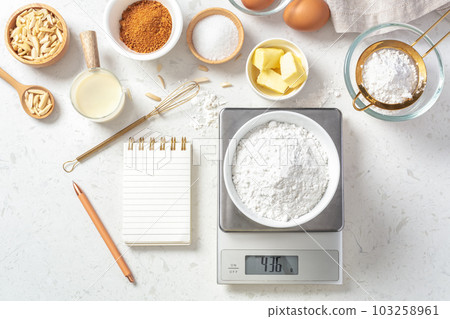 Flour in white bowl measuring on digital scale with baking ingredients and  utensil on marble kitchen table Stock Photo