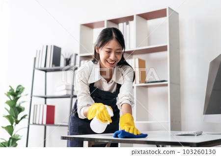 Housewife in apron wearing gloves to spraying hygiene spray on c 103260130
