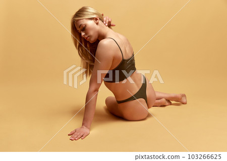 Beautiful, young, blonde woman with fit, slim figure, body posing in green underwear against yellow studio background Beautiful, young, blonde woman with fit, slim figure, body posing in green underwear against yellow studio background 103266625