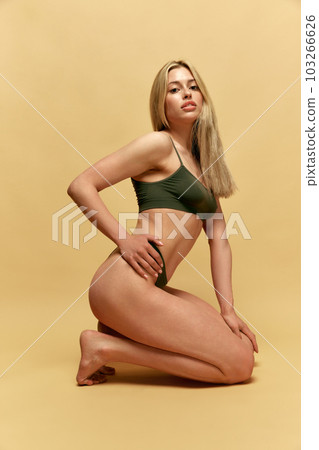 Body-positivity. Beautiful, young, blonde woman with fit, slim figure, body posing in green underwear against yellow studio background Body-positivity. Beautiful, young, blonde woman with fit, slim figure, body posing in green underwear against yellow studio background 103266626