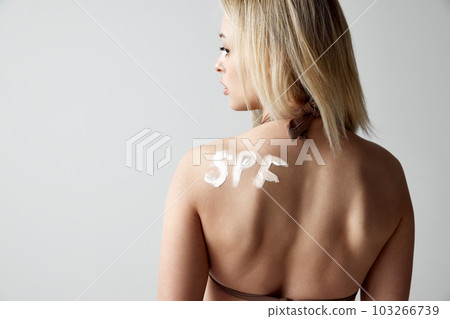 Back view image of female tanned body, shoulders with spf sunscreen protection, cream on body. Model against grey studio background 103266739