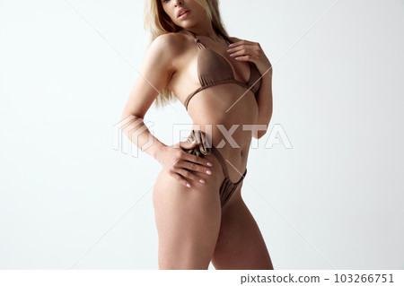 Cropped image of young, sensual woman with slim, fit body posing in swimsuit against grey studio background Cropped image of young, sensual woman with slim, fit body posing in swimsuit against grey studio background 103266751