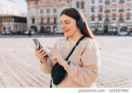 Closeup portrait of a lovely young girl listening to music through wireless earphones on urban background. Music lover enjoying music. Closeup portrait of a lovely young girl listening to music through wireless earphones on urban background. Music lover enjoying music. 103267962