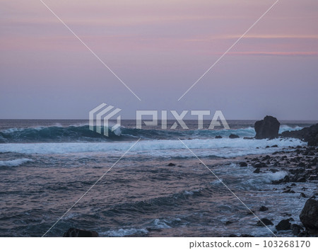 Scenic view of pink sunset on the volcanic sand beach Playa del Ingles in Valle Gran Rey, La Gomera, Canary Islands, Spain, Europe. Blue green waves are crushing, stones in the foreground 103268170