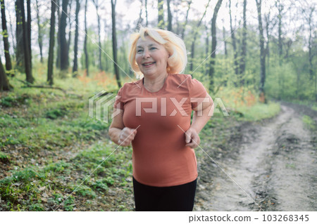 Portrait of a happy active beautiful senior caucasian woman running outdoors in nature. Active sports people. Exercise, mockup and workout with a mature female runner or athlete training outdoor in Portrait of a happy active beautiful senior caucasian woman running outdoors in nature. Active sports people. Exercise, mockup and workout with a mature female runner or athlete training outdoor in 103268345