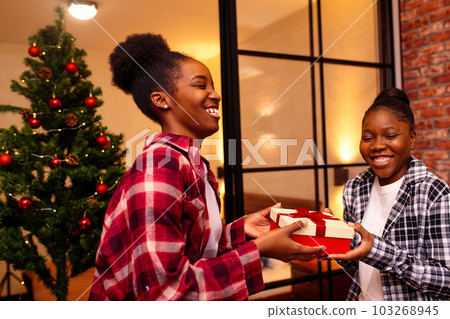 happy woman is making christmas gift to her beloved girlfriend at home at christmas night 103268945