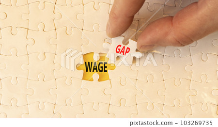 Wage gap symbol. Concept words Wage gap on beautiful white puzzles on a beautiful white background. Businessman hand. Business, support and wage gap concept. Copy space. Wage gap symbol. Concept words Wage gap on beautiful white puzzles on a beautiful white background. Businessman hand. Business, support and wage gap concept. Copy space. 103269735