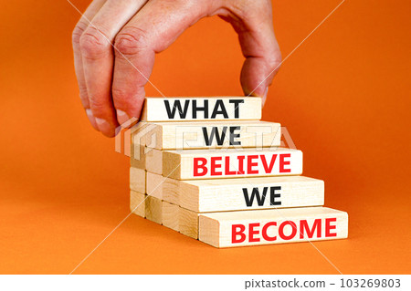 We become or believe symbol. Concept word What we believe We become on wooden block. Beautiful orange table orange background. Businessman hand. Business we become or believe concept. Copy space. 103269803