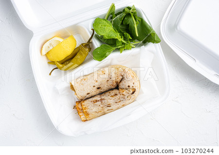 Doner kebab wrap in lavash bread, in plastic pack container delivery lunch box, on white stone table background, top view flat lay Doner kebab wrap in lavash bread, in plastic pack container delivery lunch box, on white stone table background, top view flat lay 103270244