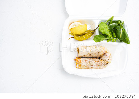 Street food chicken tantuni Turkish doner, in plastic pack container delivery lunch box, on white stone table background, top view flat lay, with copy space for text 103270384