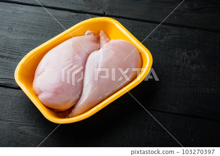 Raw chicken breast fillet in tray, on black wooden table with copy space for text 103270397