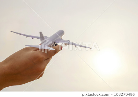 Closeup photo of woman's hand holding toy airplane against sunny sky with clouds Closeup photo of woman's hand holding toy airplane against sunny sky with clouds 103270496