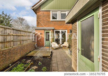 a backyard area with a wooden bench and some plants on the ground in front of a brick wall that has been painted green 103270705