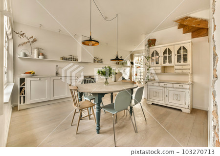 a kitchen and dining area in a house with white cabinets, wood floors and an island table surrounded by blue chairs a kitchen and dining area in a house with white cabinets, wood floors and an island table surrounded by blue chairs 103270713